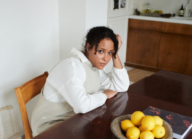 Woman wearing a white linen shirt and a pinafore linen apron layered on top