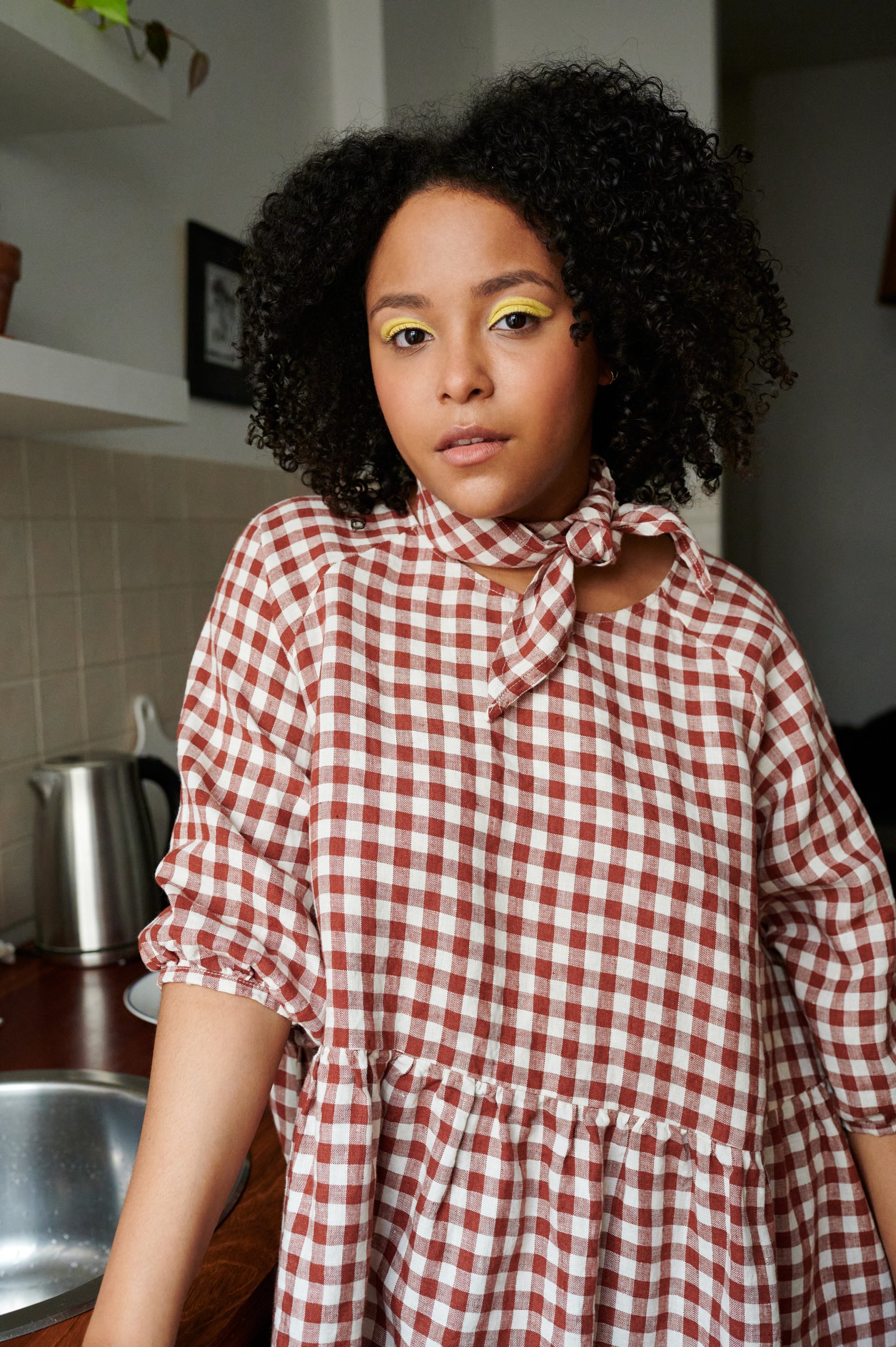 Model in a t terracotta gingham pattern oversized linen dress with three-quarter sleeves paired with a matching linen bandana tied around the neck