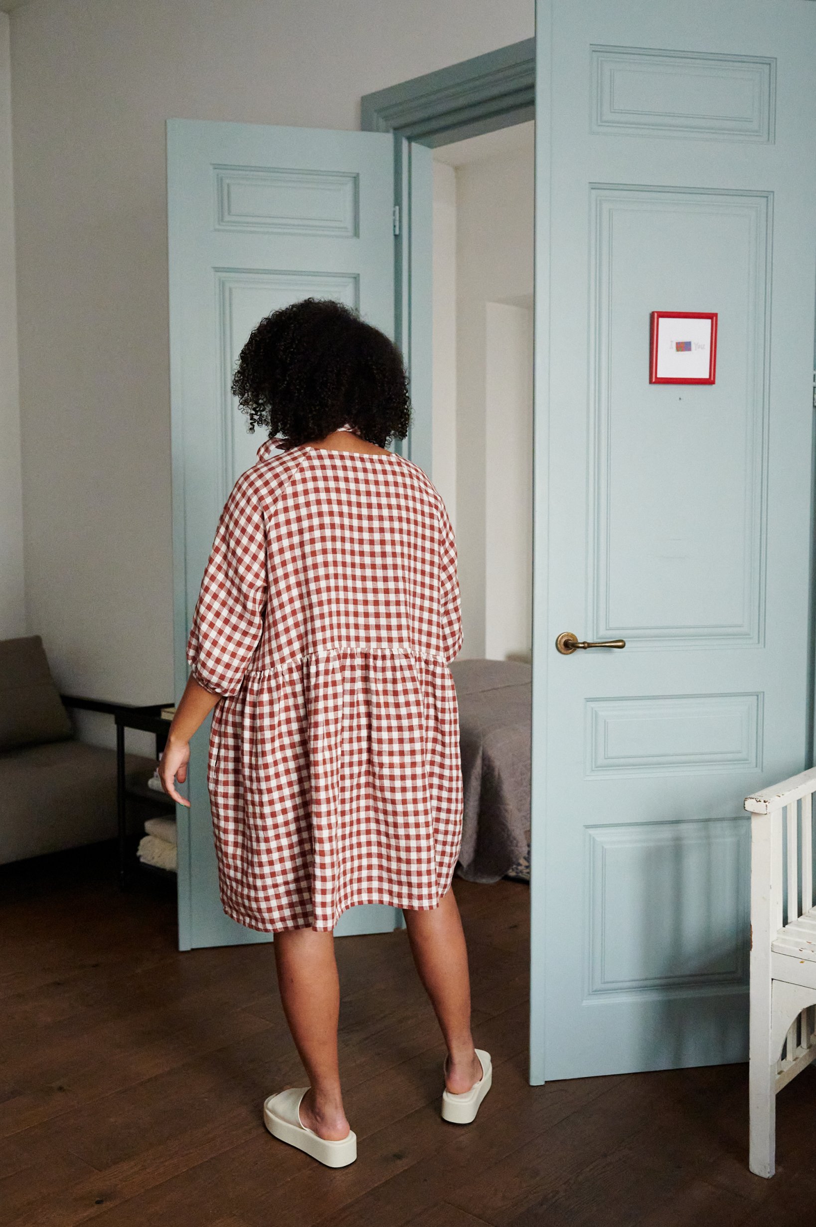 Back of a model wearing a terractota gingham oversized linen dress with a flowy skirt