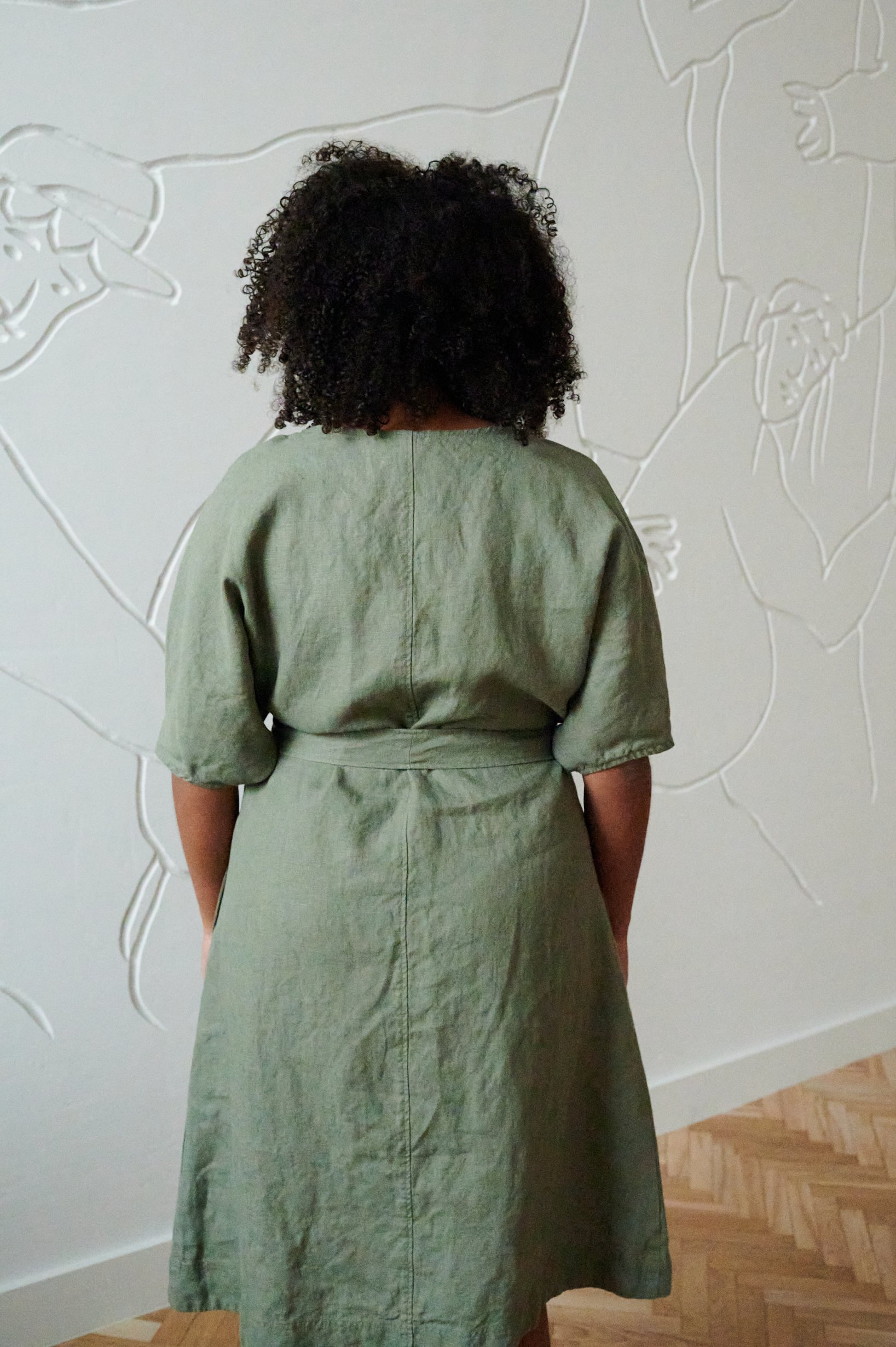 Back of a woman wearing an oversized green linen dress tied with a matching linen belt