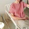 A woman sitting in red gingham short sleeve linen top