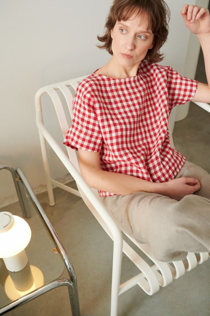 A woman sitting in red gingham short sleeve linen top