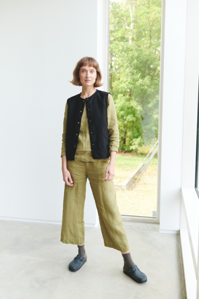 Woman wearing a black linen vest paired with olive loose-fitting linen trousers and a long sleeve linen top
