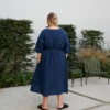 Back of a woman in mid-length loose-fitting linen dress with a belt and wide sleeves