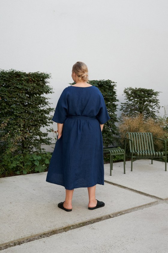 Back of a woman in mid-length loose-fitting linen dress with a belt and wide sleeves