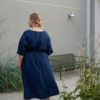 Back of a model in a loose-fitting navy blue linen dress with a matching belt
