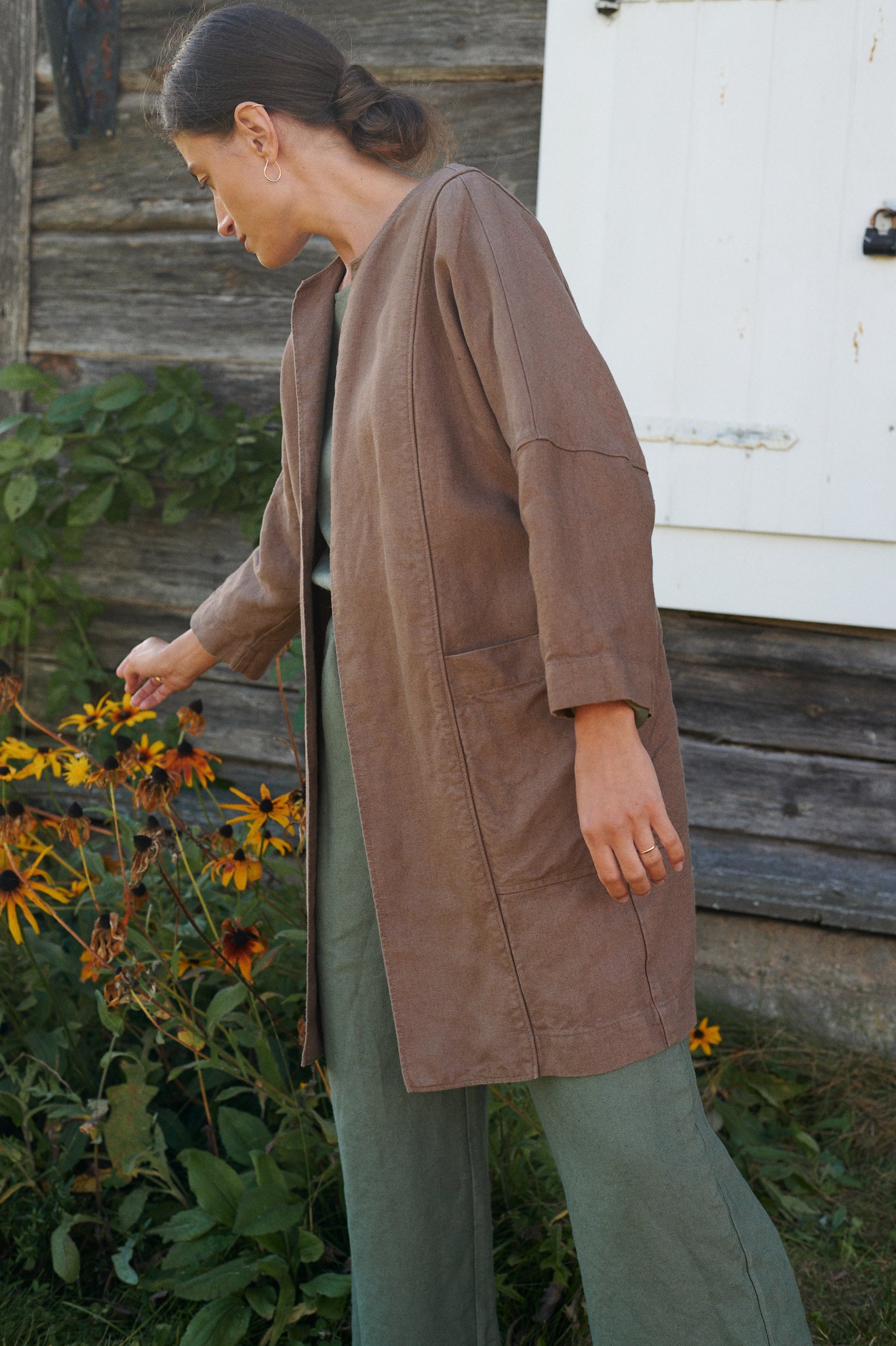 Side view of model wearing a loose-fitting brown linen jacket paired with green linen pants