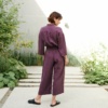 Back of a model in a violet linen jumpsuit with wide, lightly cropped legs