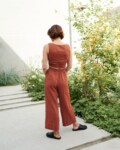 Model is wearing wide leg linen trousers in terracotta color
