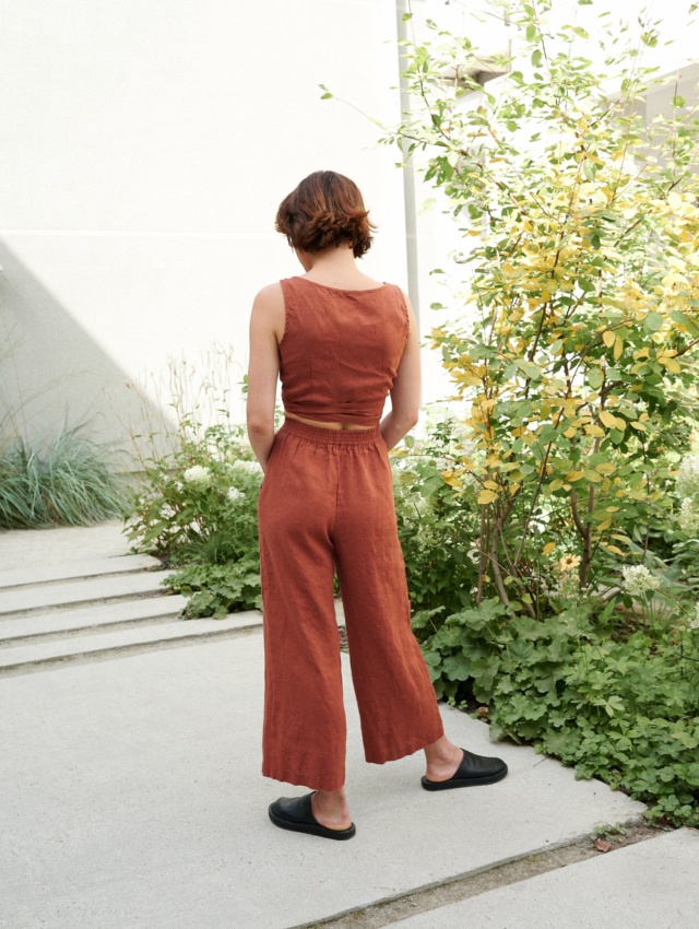 Model is wearing wide leg linen trousers in terracotta color