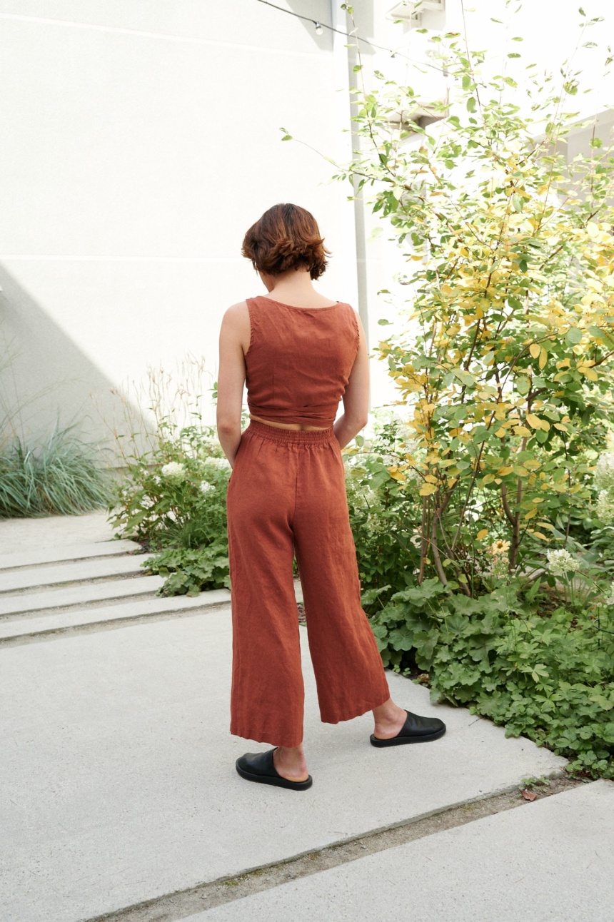 Model is wearing wide leg linen trousers in terracotta color