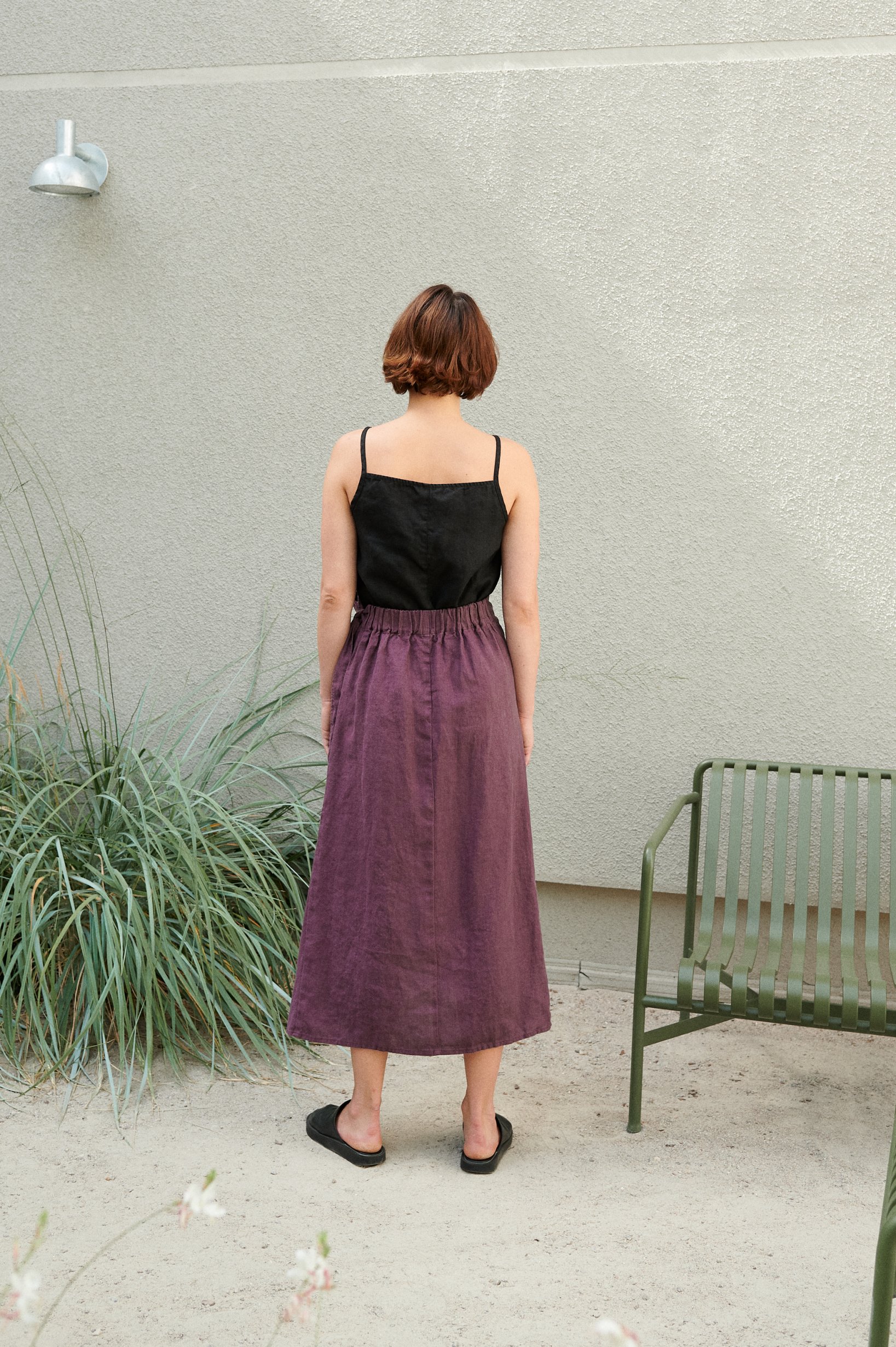 Back of a model in a long linen skirt with a black spaghetti strap linen top tucked into it