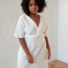 Model in a while linen dress with a V-neckline and a twist in the front