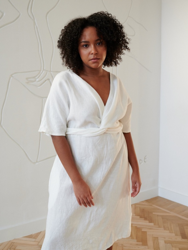 Model in a while linen dress with a V-neckline and a twist in the front