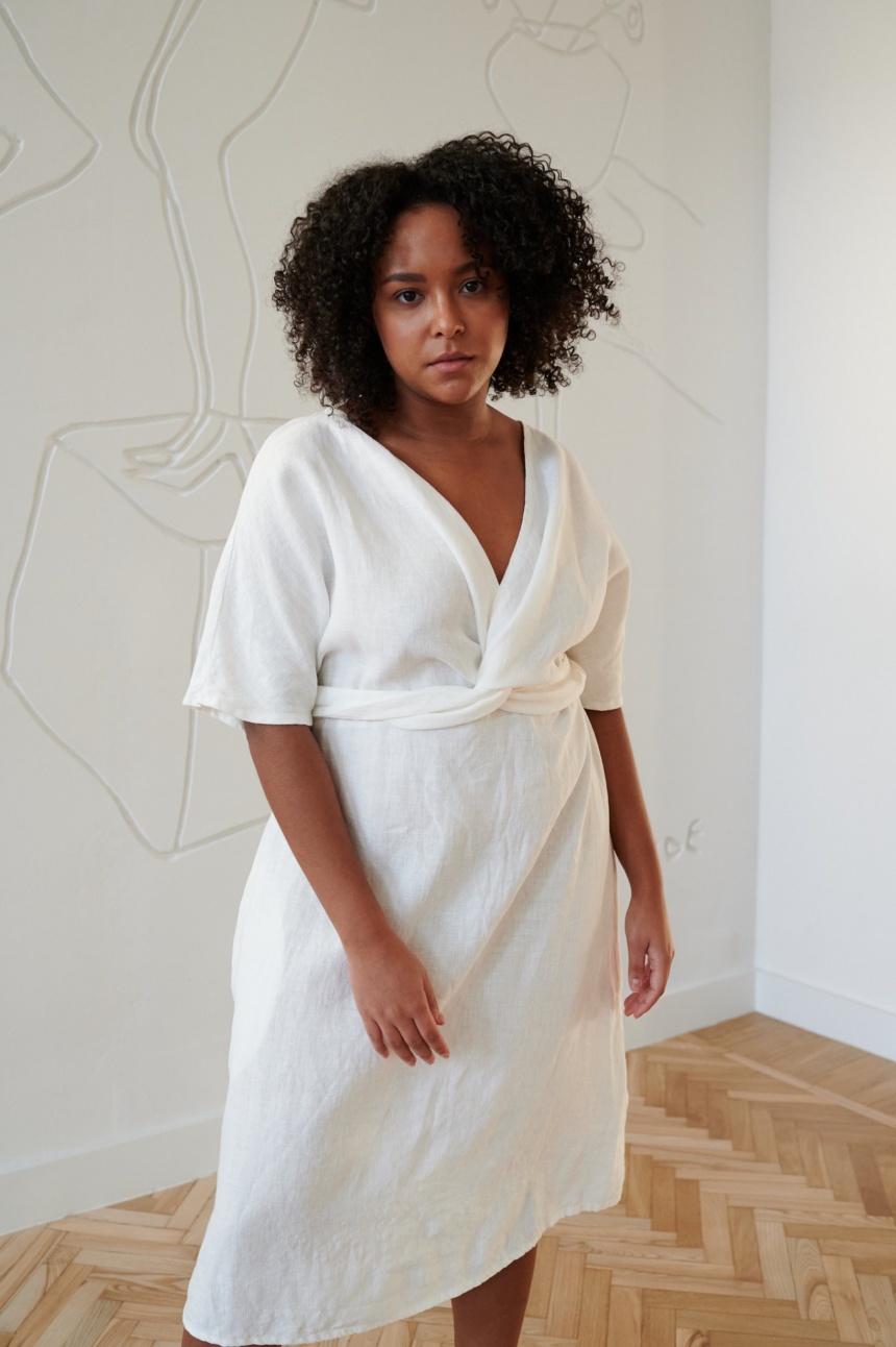 Model in a while linen dress with a V-neckline and a twist in the front