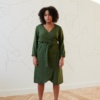 Front of a model in a forest green wrap linen dress with long sleeves and a medium length hem