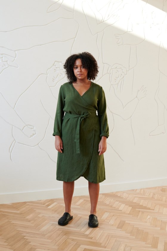 Front of a model in a forest green wrap linen dress with long sleeves and a medium length hem
