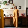 A woman standing in barrel leg linen trousers in mustard yellow