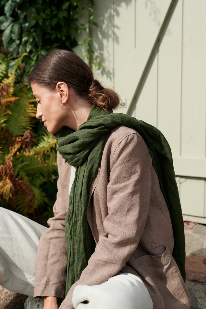 Side view of a model sitting while wearing a forest green linen scarf in a linen outfit