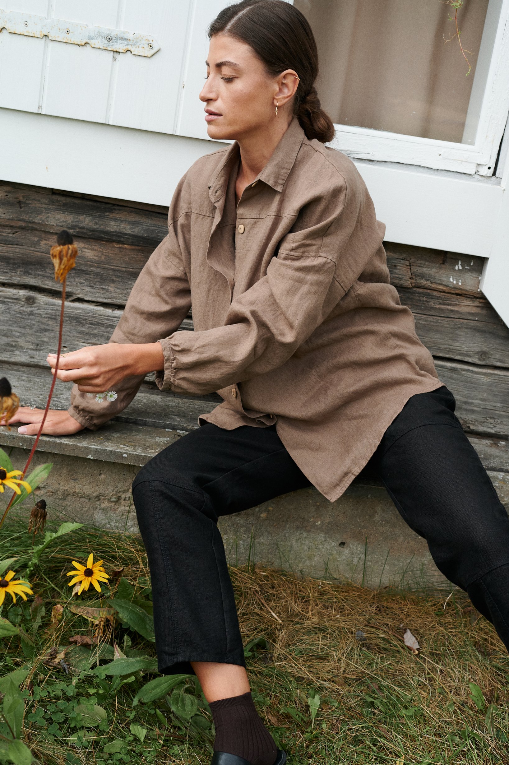 A woman sitting in loose-fitting linen brown button down