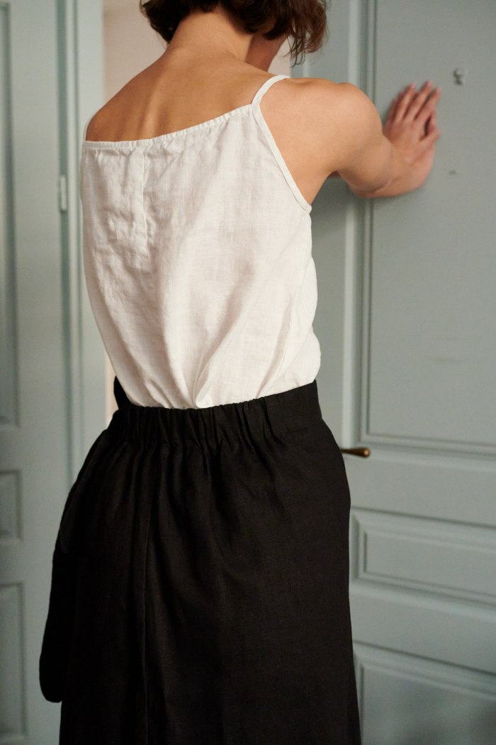A lightweight white linen summer top tucked into the waistband of black linen trousers