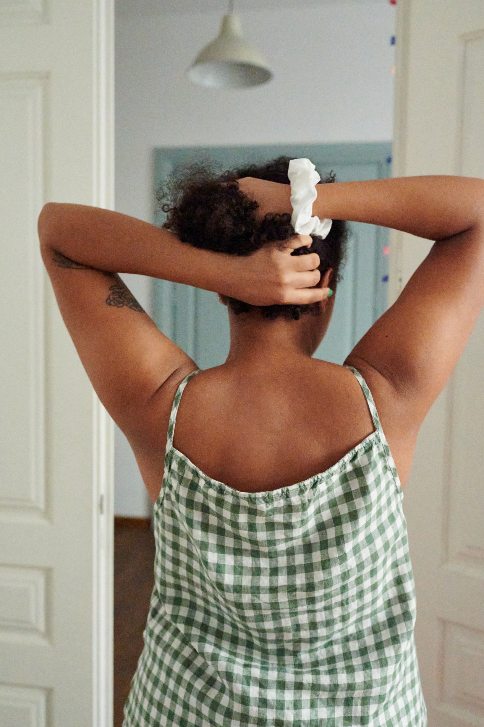 Model tying up her hair with a linen scrunchie while wearing a green gingham linen summer top