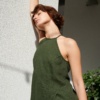 Model leaning against a wall while wearing a green lightweight linen dress with an asymmetrical seam