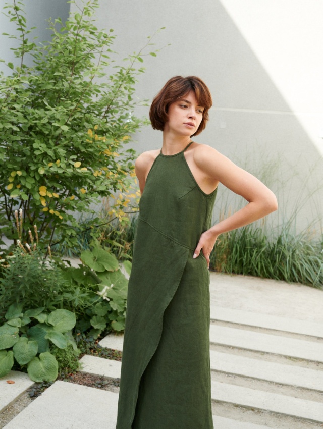 Model posing in a long forest green linen dress with an asymmetrical seam