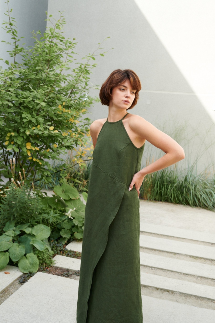 Model posing in a long forest green linen dress with an asymmetrical seam