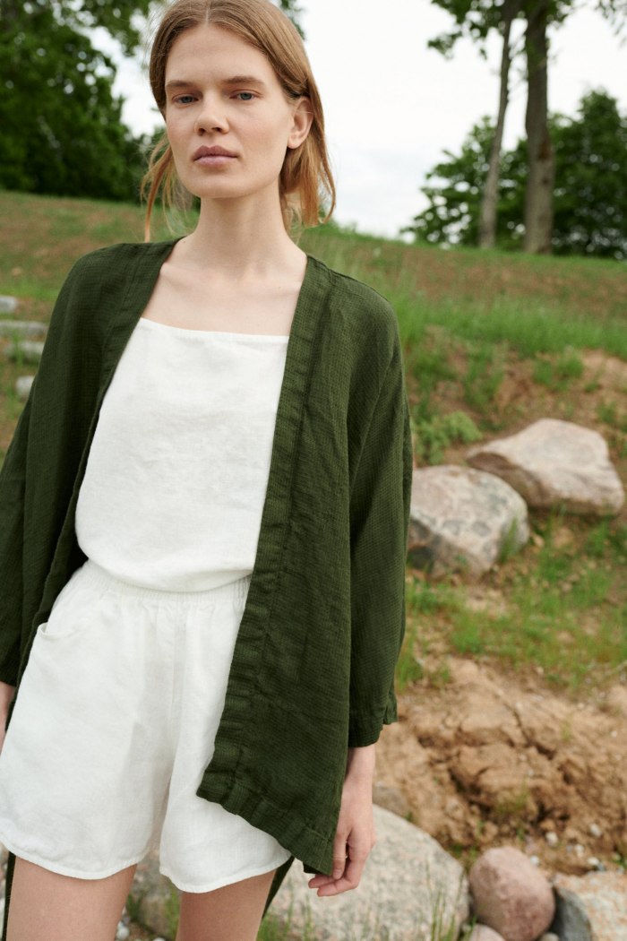 Woman wearing a green waffle linen jacket untied with a white linen summer top underneath