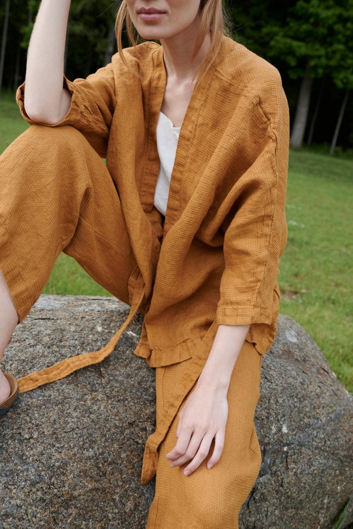 A woman sitting down while wearing a loose waffle linen jacket and matching linen trousers