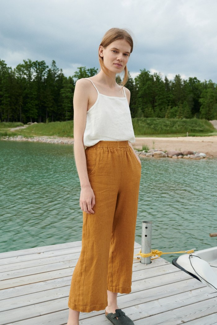 A woman standing in relaxed fit waffle linen trousers in camel