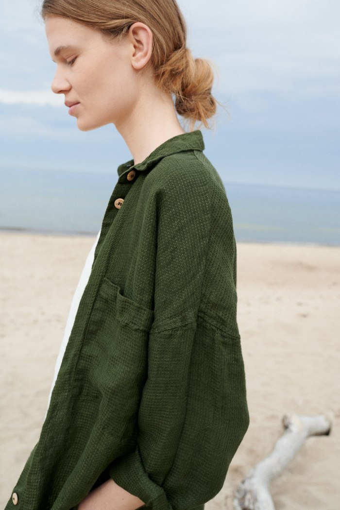 Side view of a woman in an oversized forest green waffle linen button down shirt