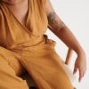 Woman sitting while wearing a camel linen jumpsuit with a V-neckline
