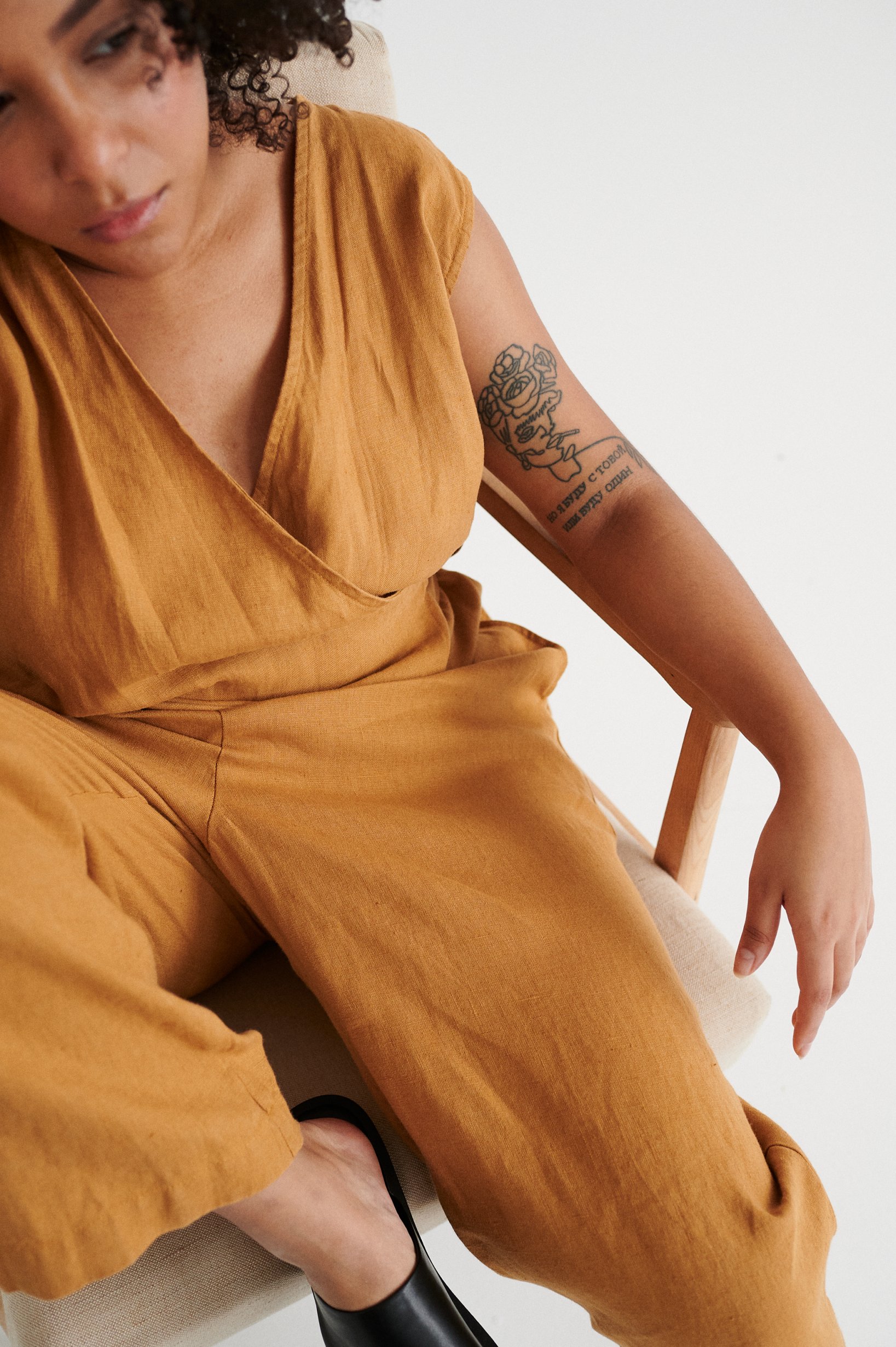 Woman sitting while wearing a camel linen jumpsuit with a V-neckline