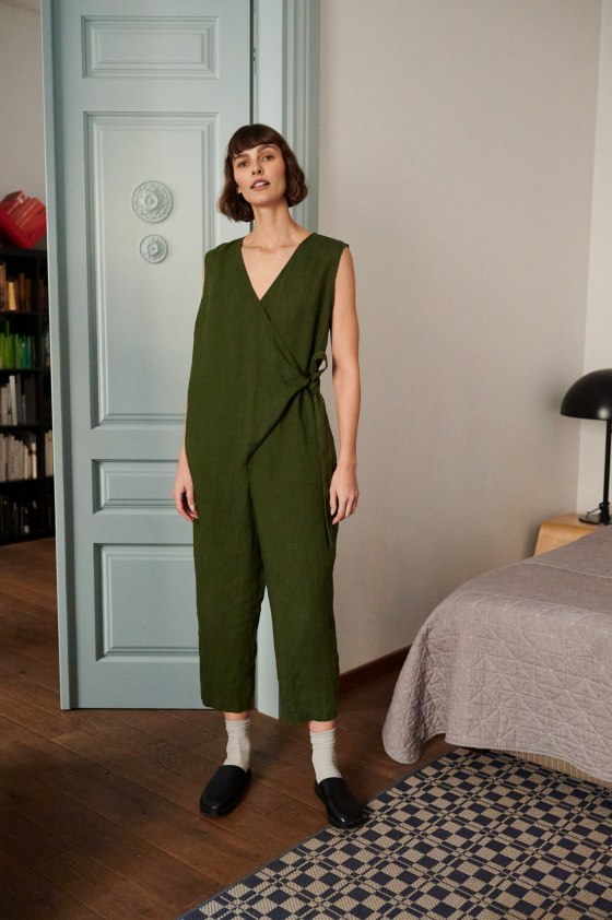 A model wearing an oversized dark green linen jumpsuit with a wrap top and a belt tied on the side