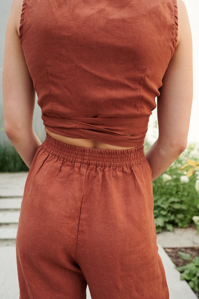 An elasticated waistband of terracotta linen trousers and a cropped linen top