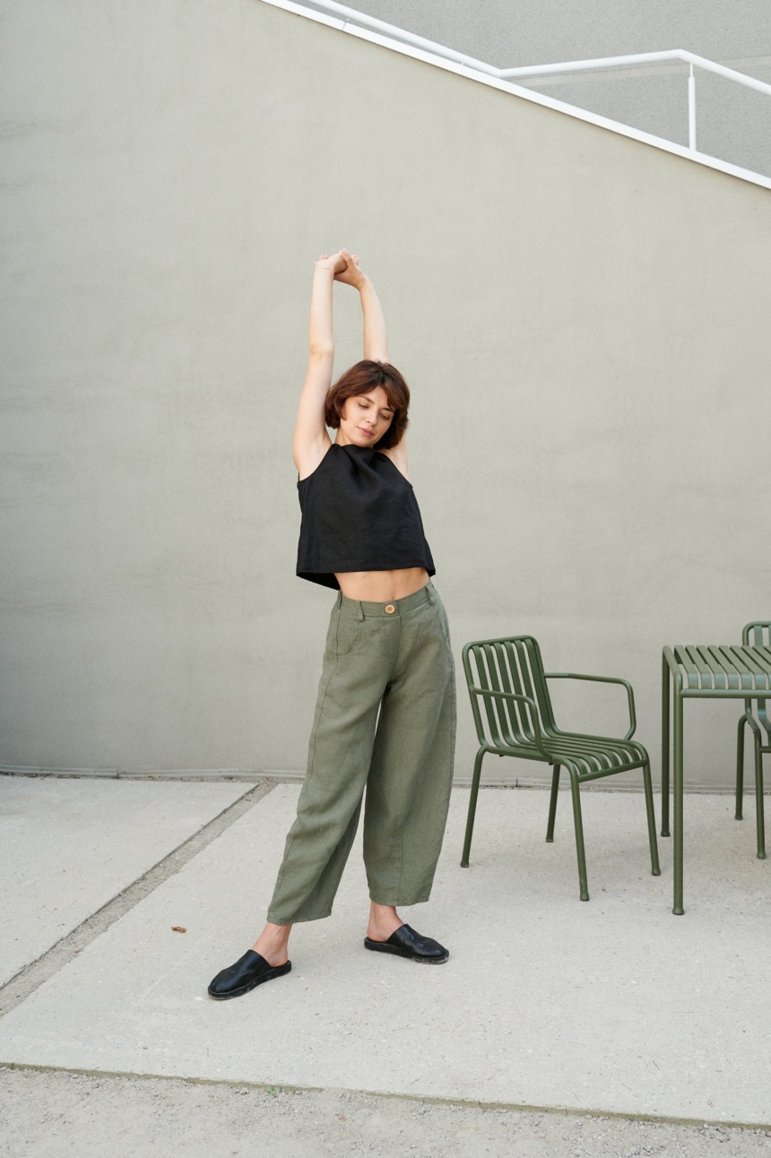 A woman stretching in heavy linen barrel trousers in green