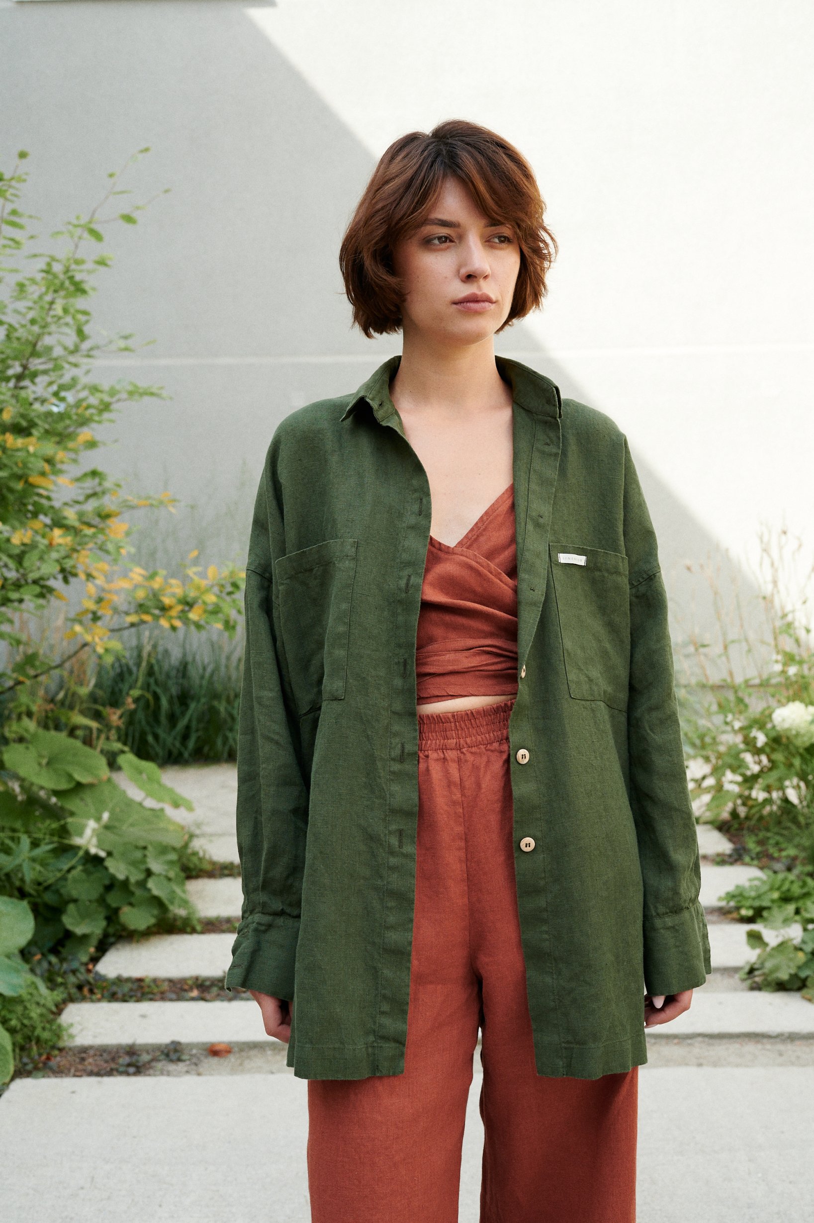 Woman in a loose-fitting green button down linen shirt and terracotta linen top and trousers outfit