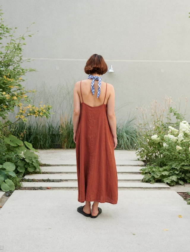 Back of a model wearing a long linen summer dress with a low-cut back and thin straps