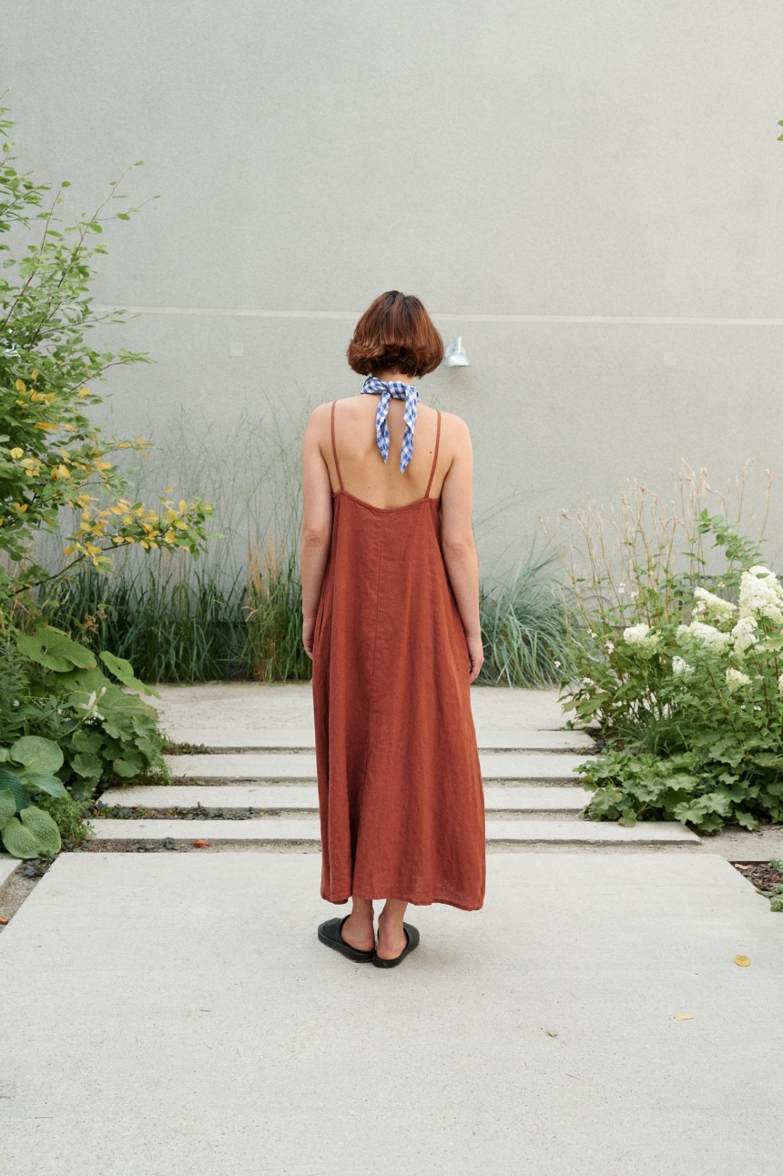 Back of a model wearing a long linen summer dress with a low-cut back and thin straps