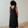 Back of a model in a long black linen dress with a V neckline in the back