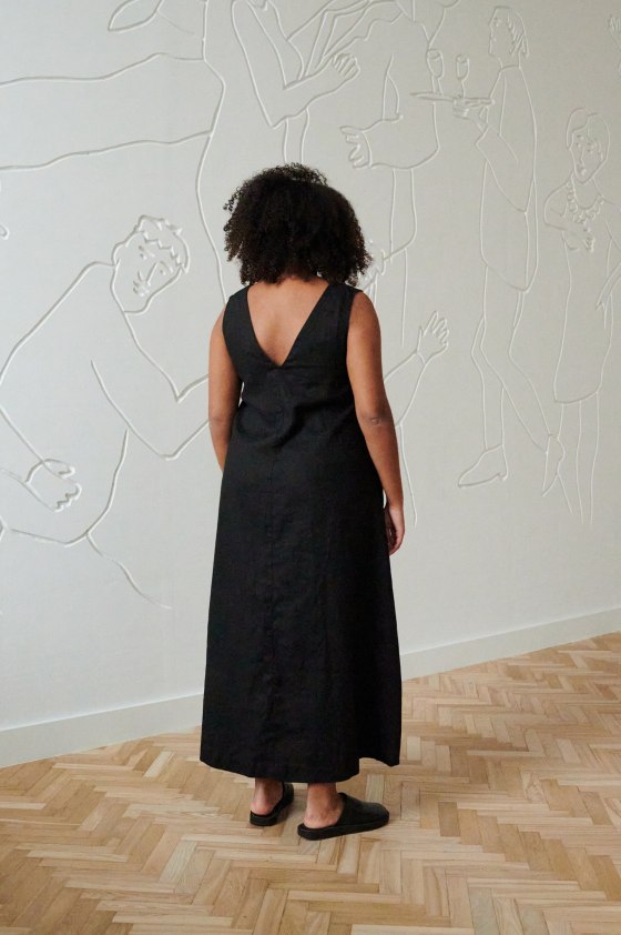 Back of a model in a long black linen dress with a V neckline in the back