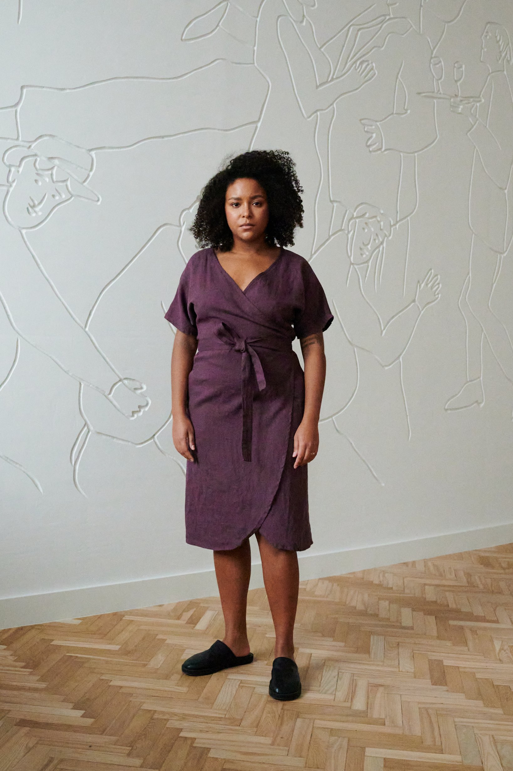 Model in a dark purple wrap linen dress with dropped sleeves and medium length hem