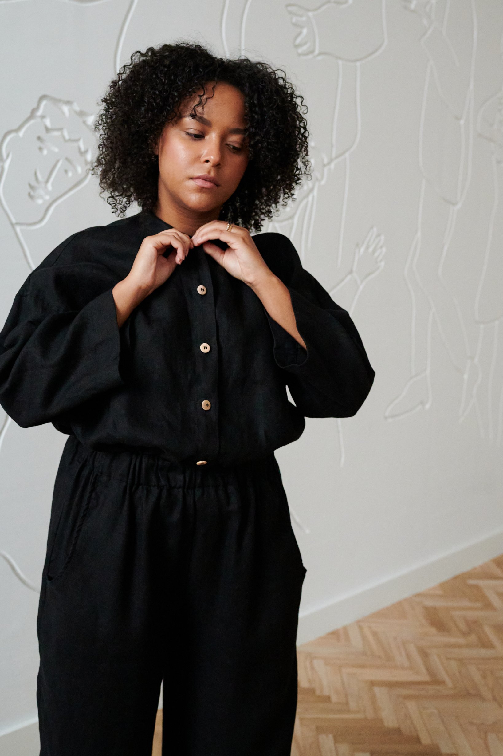 A woman buttoning up linen shirt in black