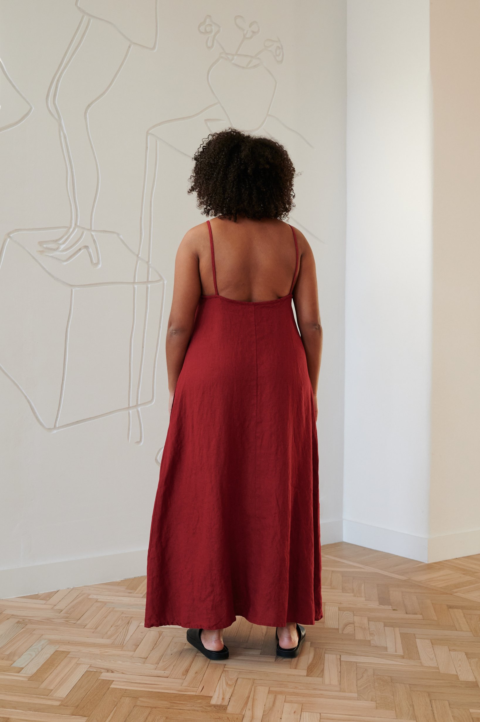 Back of a model wearing a red flared maxi linen dress with a low-cut back and spaghetti straps