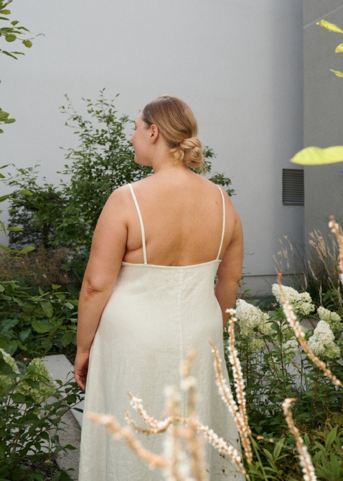 The back of a model in a white linen dress with thin straps