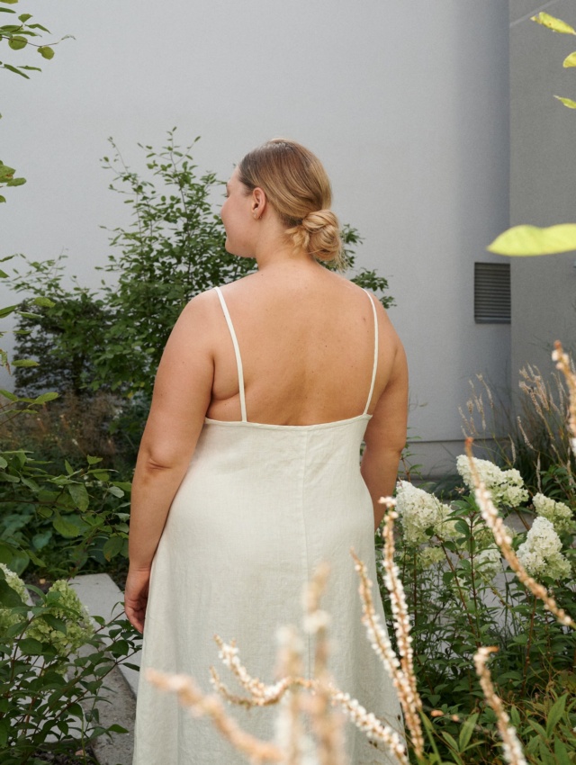 The back of a model in a white linen dress with thin straps