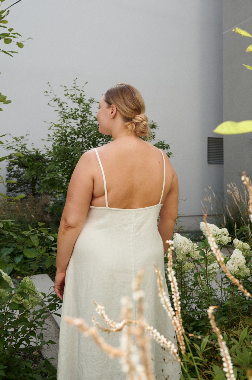 The back of a model in a white linen dress with thin straps