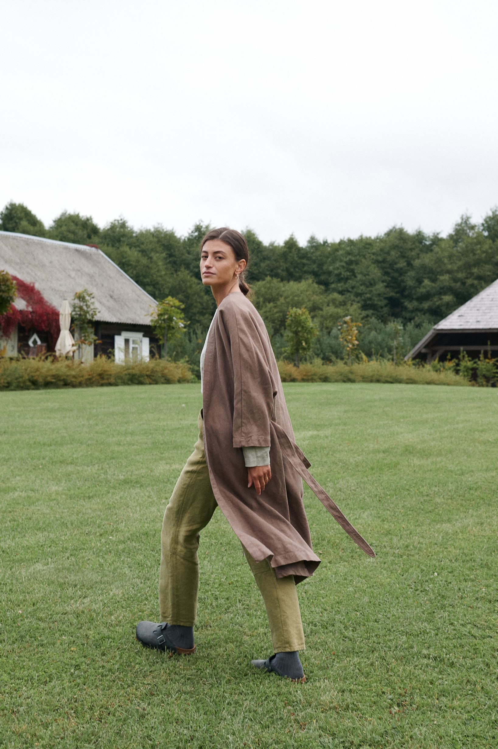 A model wearing a long brown linen jacket that's flowing as she's walking